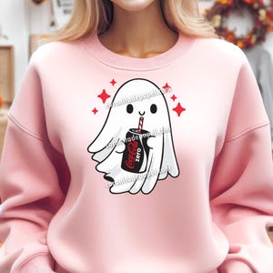 Puede incluir: Sudadera rosa claro con un dise&ntilde;o de fantasma de dibujos animados. El fantasma blanco sostiene una lata de Coca-Cola Zero con una pajita roja y blanca. Estallidos de estrellas rojas rodean al fantasma. El texto "coronitadepapel.com" es visible.
