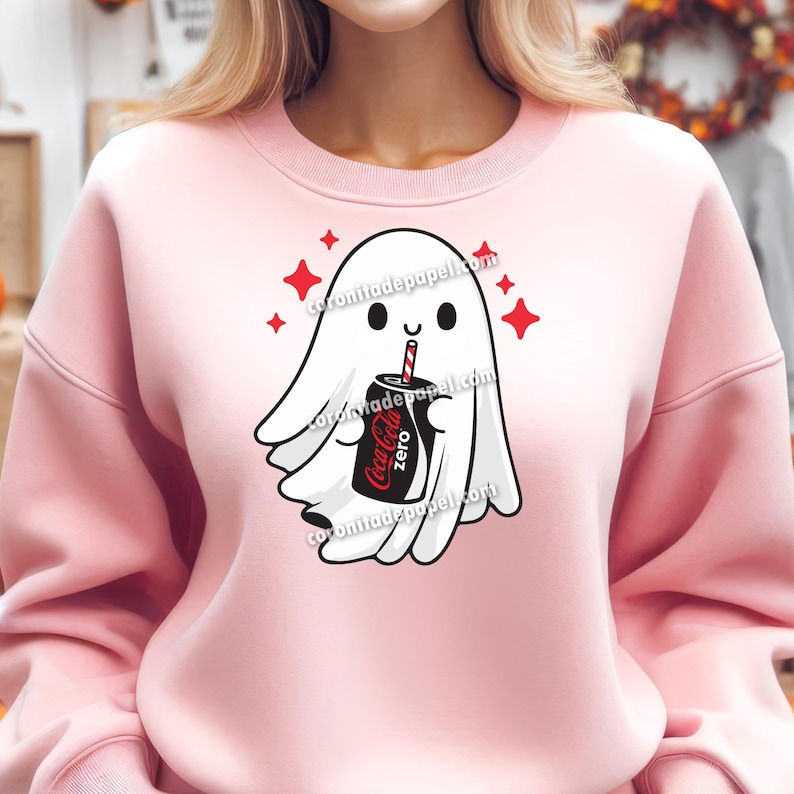 Puede incluir: Sudadera rosa claro con un dise&ntilde;o de fantasma de dibujos animados. El fantasma blanco sostiene una lata de Coca-Cola Zero con una pajita roja y blanca. Estallidos de estrellas rojas rodean al fantasma. El texto "coronitadepapel.com" es visible.