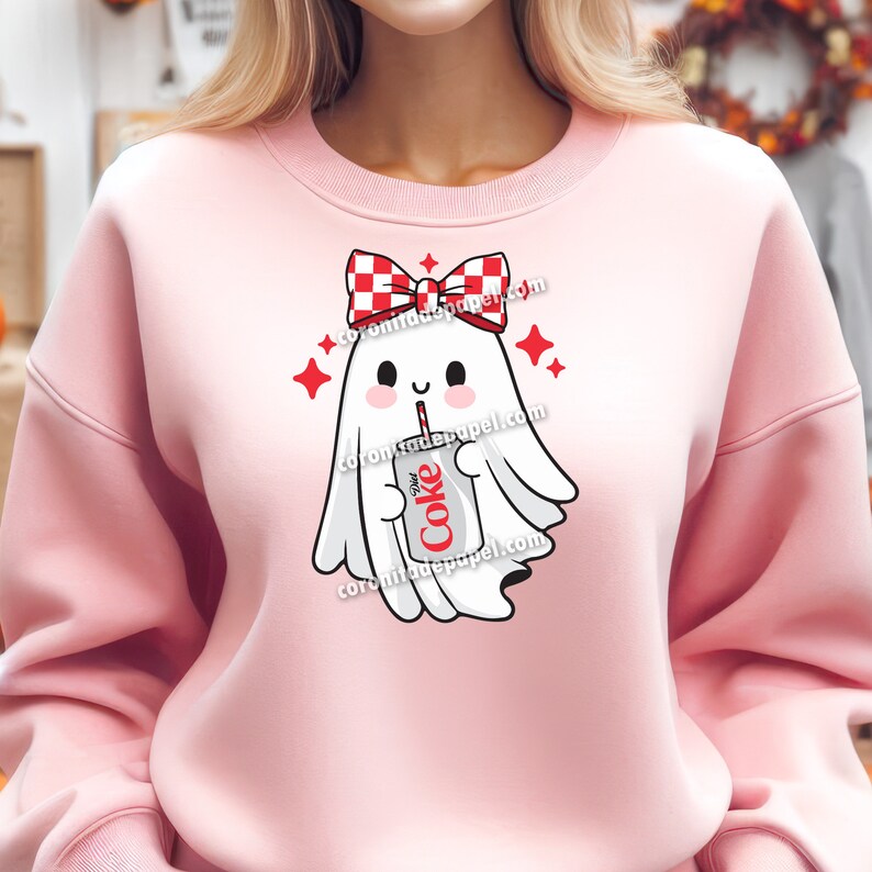 May include: Pink sweatshirt featuring a cute ghost graphic. The ghost wears a red and white checkered bow and holds a Diet Coke can with a straw. Red star accents surround the ghost. The text "Diet Coke" is visible on the can.