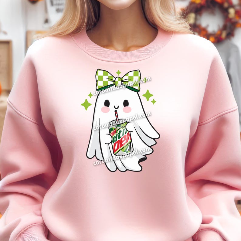 May include: A light pink sweatshirt featuring a cartoon ghost with a green and white checkered bow, holding a Mountain Dew can with a straw. The ghost has a cute expression and is surrounded by green star accents.