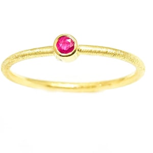 Peut inclure: Une délicate bague en or avec une petite pierre précieuse de rubis rouge vif sertie au centre.