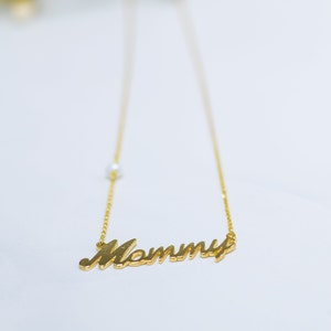 May include: A gold necklace with a cursive 'Mommy' pendant and a single pearl accent.