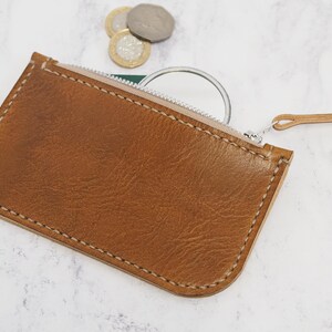 May include: A brown leather zippered pouch with a white zipper and a small, round mirror inside.