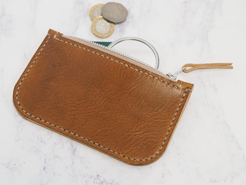 May include: A brown leather zippered pouch with a white zipper and a small, round mirror inside.