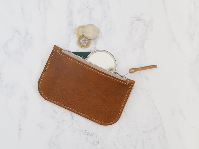May include: A brown leather zippered pouch with a small round mirror inside. The pouch is open and the zipper pull is visible.