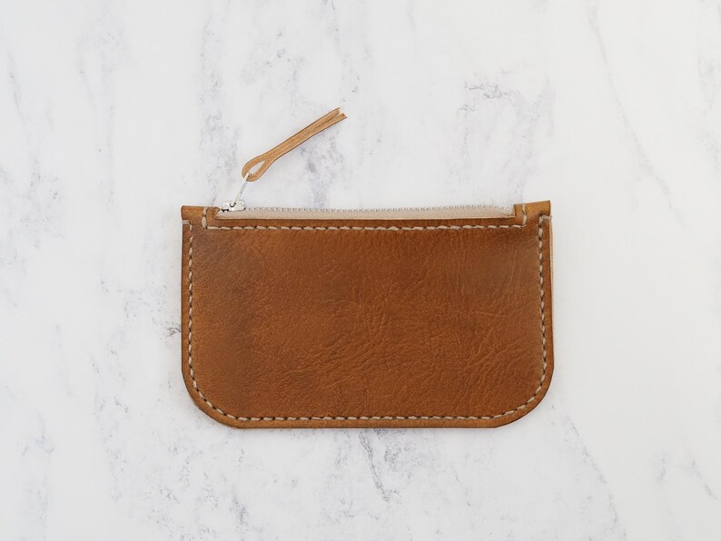 May include: A small brown leather zipper pouch with a light brown zipper pull.