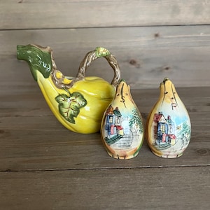May include: A set of three yellow ceramic salt and pepper shakers shaped like gourds. The shakers are decorated with a painted scene of a small town with houses and trees. The salt shaker is labeled "S" and the pepper shaker is labeled "P".