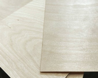 May include: Close-up of several sheets of light-colored plywood. The wood grain is visible, and the sheets are stacked at different angles, showcasing the natural wood tones and textures. The plywood appears to be new and unused.