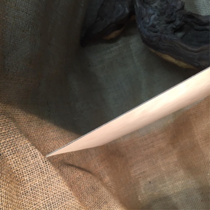 Op de afbeelding: Een close-up van een lichtbruine jute stof met een dun, zilveren metalen blad erop.