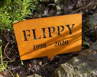 Op de afbeelding: Een roestige bruine metalen gedenkplaat met de naam "Flippy" en de data "1998 - 2020" erop gegraveerd.