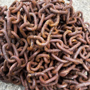 May include: Close-up of a pile of rusty metal chains. The chains are a deep brown color with areas of orange rust. The links are interlocked, creating a dense, textured pattern. The image suggests a vintage or industrial theme.