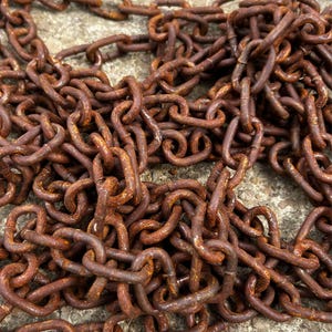 May include: Close-up of a pile of rusty metal chains. The chains are a deep reddish-brown color, with visible rust and wear. The links are interlocked, creating a dense, textured pattern. The image suggests a vintage or industrial theme.