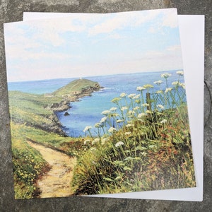 May include: A landscape art print depicting a coastal scene with a path leading to the sea. The print features a blue sky, green hills, and white flowers in the foreground. A white card is visible.