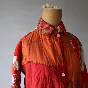 Puede incluir: Una camisa de retazos roja y naranja con un cuello de estampado floral. La camisa está hecha de diferentes telas y tiene costuras visibles.