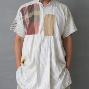 以下が含まれることがあります： ストライプ柄の白の半袖シャツ、パッチワークのディテール付き。 シャツはスタンドカラーで、赤、茶色、ベージュのパッチが付いています。 カーキ色のパンツと合わせています。