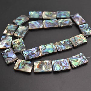 May include: A strand of iridescent abalone shell beads, each bead is a rectangular shape with a unique pattern of blue, green, and gold colors. The beads are strung on a clear elastic cord.