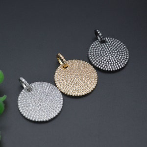 May include: Three round pendants with a pave setting of small, sparkling stones. One pendant is gold-toned, one is silver-toned, and the third is dark gray. Each pendant has a small loop at the top for a chain.