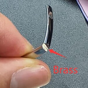 May include: Close-up of a curved, silver-colored metal object with a small hole. The end of the object has a brass-colored section. The word "Brass" is written in red text near the object.