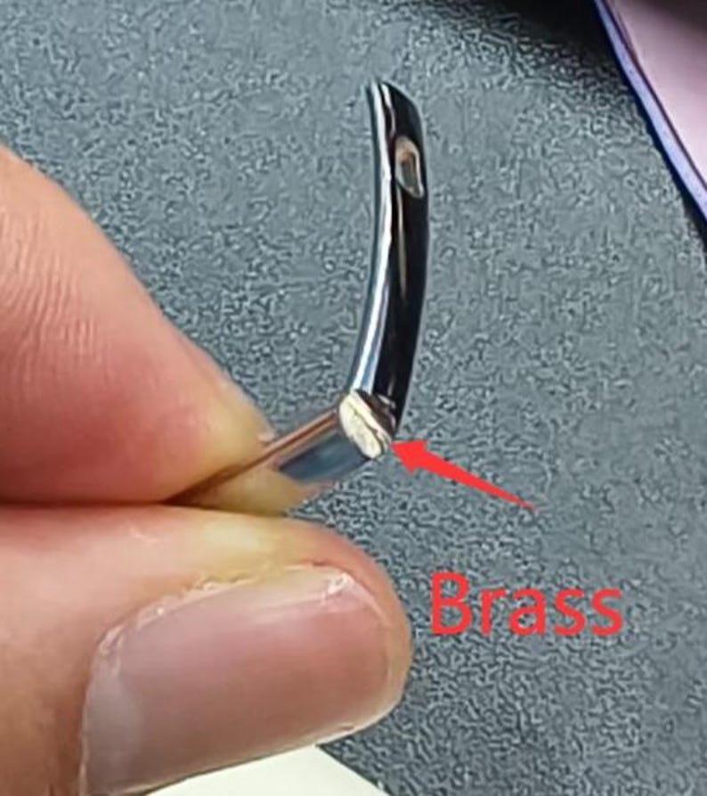 May include: Close-up of a curved, silver-colored metal object with a small hole. The end of the object has a brass-colored section. The word "Brass" is written in red text near the object.