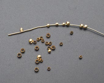 May include: A selection of small, gold-coloured jewellery-making supplies. The image shows various beads, including round and donut-shaped beads, along with a thin wire. The beads are scattered on a dark grey surface.