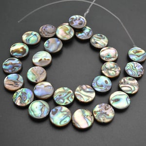 May include: A strand of round, iridescent abalone shell beads. The beads are strung on a clear thread and have a variety of colours, including green, blue, and brown.