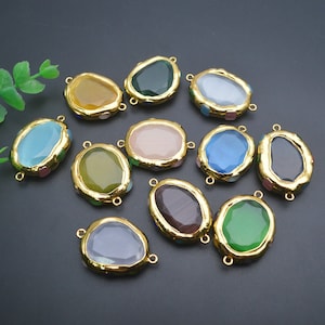 May include: Assortment of 12 oval-shaped glass charms with gold-tone metal frames. Each charm features a different color glass insert, including blue, green, pink, and brown.