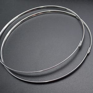 May include: Two silver-colored, thin metal necklaces or chokers, each forming a complete circle. The necklaces are slightly overlapping, with a simple clasp visible on each. The background is a solid, dark gray.