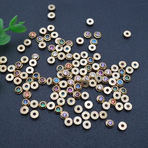 May include: A large group of gold-coloured metal beads with colourful rhinestones in the centre. The beads are scattered on a dark grey surface.