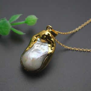 May include: A gold chain necklace with a large, irregular, white pearl pendant. The pearl is set in a gold frame.