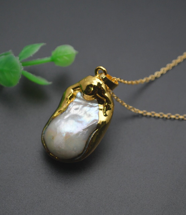 May include: A gold chain necklace with a large, irregular, white pearl pendant. The pearl is set in a gold frame.