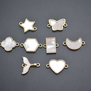 May include: Assortment of eight gold-toned metal charms with white shell inlays. The charms are shaped like a star, butterfly, four-leaf clover, hexagon, rectangle, crescent moon, mermaid tail, and heart.