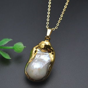May include: A gold chain necklace with a large, irregular-shaped pearl pendant. The pearl is white and has a gold-toned setting.