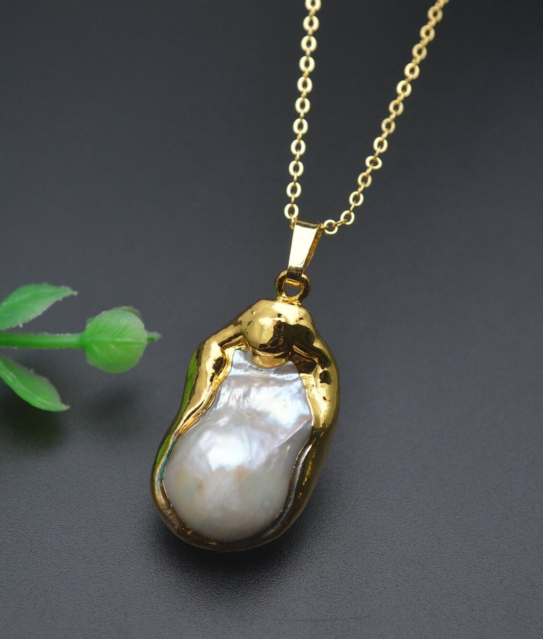 May include: A gold chain necklace with a large, irregular-shaped pearl pendant. The pearl is white and has a gold-toned setting.