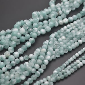 May include: Strands of round, pale blue-green gemstone beads. The beads vary in size, with larger beads at the top and smaller ones at the bottom. The beads have a marbled appearance.