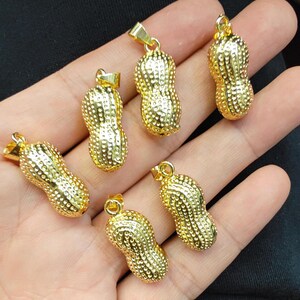 May include: Six gold peanut-shaped pendants with a textured surface. The pendants have a loop at the top for attaching to a chain.