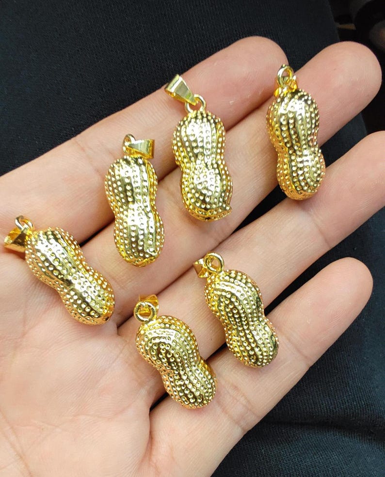 May include: Six gold peanut-shaped pendants with a textured surface. The pendants have a loop at the top for attaching to a chain.