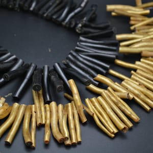 Puede incluir: Un collar hecho de ramas de coral negro y dorado. El collar está hecho de materiales naturales y tiene un aspecto rústico y orgánico.
