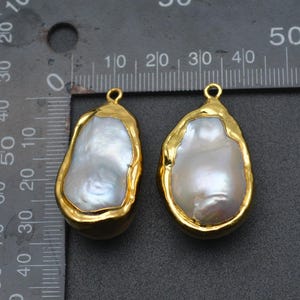 May include: Two gold-plated baroque pearl pendants with a loop at the top for hanging. The pearls are white and have an irregular shape.