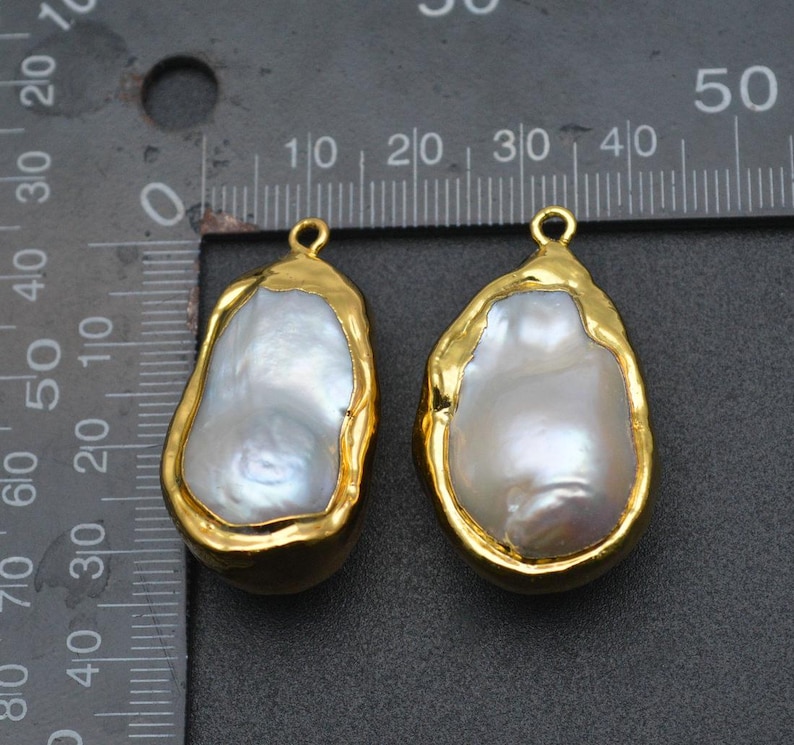 May include: Two gold-plated baroque pearl pendants with a loop at the top for hanging. The pearls are white and have an irregular shape.