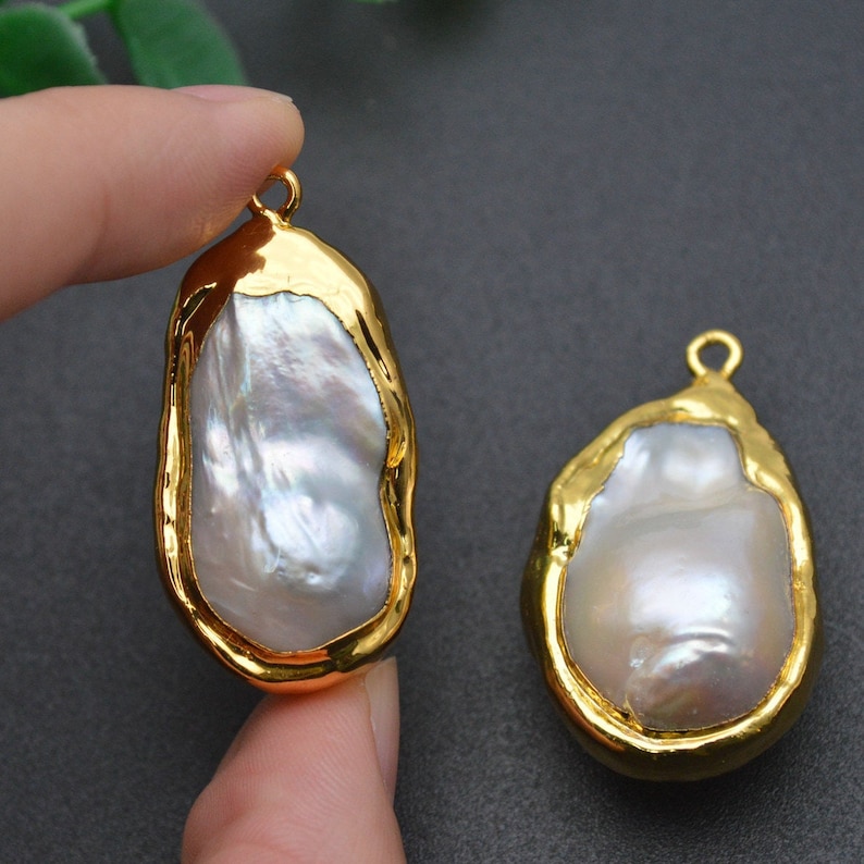 May include: Two gold-plated baroque pearl charms with a smooth, white pearl center. The charms are oval-shaped and have a slightly irregular, textured gold edge.