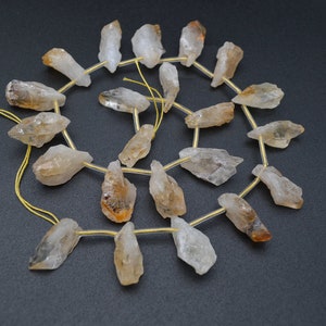 May include: A strand of raw, clear quartz crystal beads with a golden brown hue. The beads are strung on a gold wire and are approximately 1 inch in length.