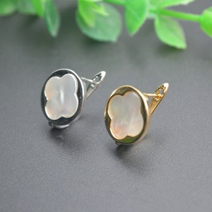 May include: Two clover-shaped earrings with a white mother-of-pearl centre. One earring has a silver-toned metal frame, and the other has a gold-toned metal frame.