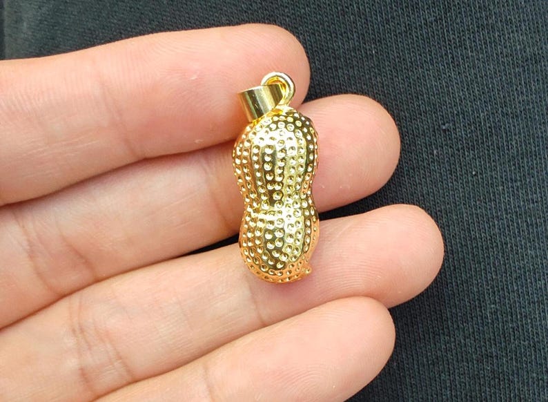May include: A gold-colored peanut-shaped pendant charm. The pendant has a textured surface and is designed to look like a peanut.