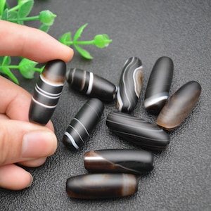 May include: A collection of eight black and white agate beads, each with a unique pattern of stripes and swirls. The beads are oval-shaped and have a smooth, polished finish.