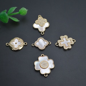 May include: Five gold-tone metal charms with white mother-of-pearl inlays and clear rhinestone accents. The charms are shaped like four-leaf clovers and a flower.