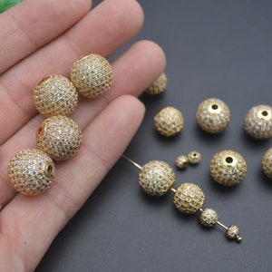 May include: A collection of gold-toned round beads with clear crystal accents. The beads have a hole in the center for stringing.