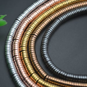 May include: A close-up of four strands of round, metal beads. The beads are in different colors: silver, rose gold, gold, and black.