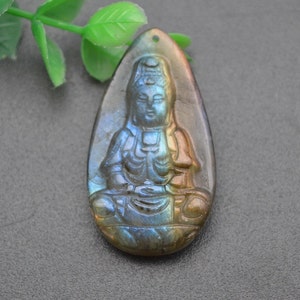 Può includere: Un ciondolo a forma di lacrima intagliato in pietra preziosa di labradorite iridescente, che presenta una rappresentazione dettagliata di una figura di Buddha seduto.