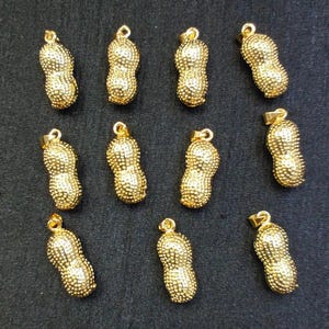 May include: Twelve gold peanut-shaped pendants with a textured surface. The pendants are all the same size and shape.