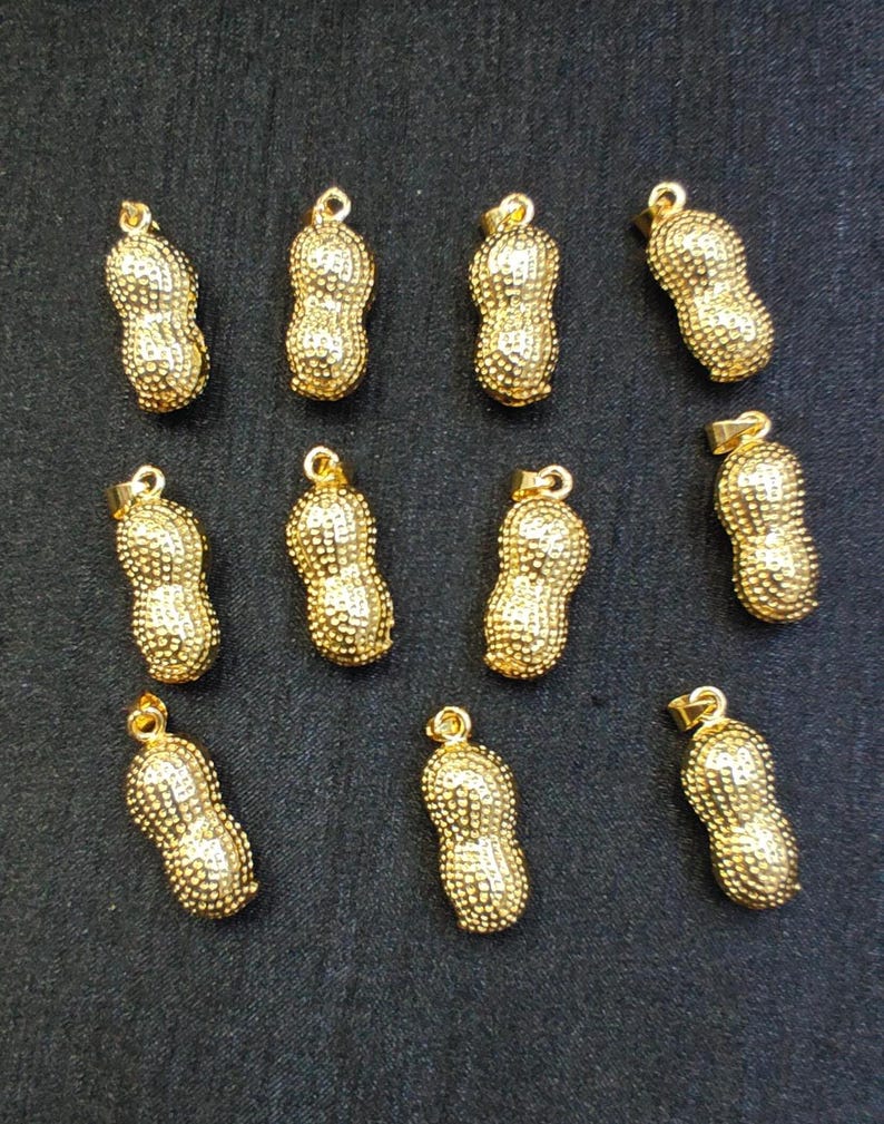 May include: Twelve gold peanut-shaped pendants with a textured surface. The pendants are all the same size and shape.